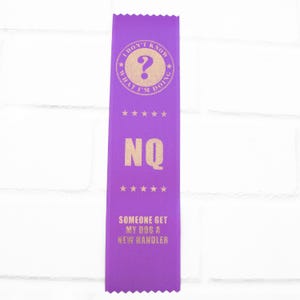 May include: A purple ribbon with gold text. The top of the ribbon has the text "I DON'T KNOW WHAT I'M DOING" around a question mark. Below are the letters "NQ" and the text "SOMEONE GET MY DOG A NEW HANDLER".