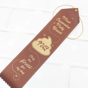 May include: A brown ribbon with gold text that reads "Most Expensive Potty Break" and "Only the finest for my dog" with a gold poop emoji in the middle.