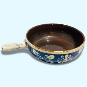 以下が含まれることがあります： 茶色の内側と白い取っ手を持つ青と白のセラミックボウル。ボウルは、青い背景に白い花と葉の入った花柄のデザインです。