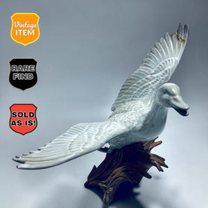 Puede incluir: Figura de pato de cerámica vintage en vuelo, con las alas extendidas. El pato es de color gris claro, posado sobre una base de madera marrón. Las alas están detalladas con patrones de plumas. El texto "Vintage Item", "Rare Find" y "Sold As Is!"
