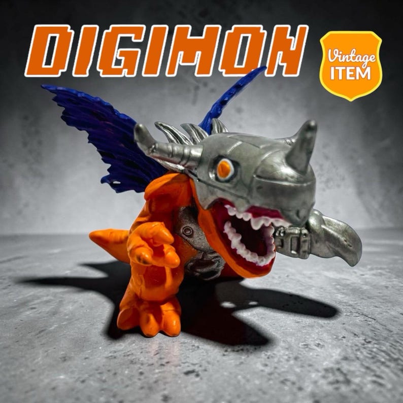 Puede incluir: Una peque&ntilde;a figura de Digimon naranja y plateada con un casco gris met&aacute;lico con cuerno, dientes blancos afilados y alas azul oscuro. El texto DIGIMON aparece en letras naranjas grandes en la parte superior, junto a un escudo amarillo VINTAGE ITEM.