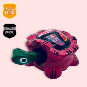 May include: A hand-painted, vintage turtle figurine with a vibrant pink shell and a green head. The shell features black, white, and blue decorative patterns. The figurine is labelled "Vintage Item" and "Rare Find".