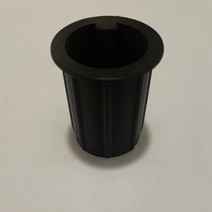 May include: Black plastic cup holder with a ribbed design. The cup holder has a lip around the top edge.