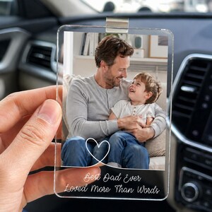 Peut inclure: Ornement de voiture en acrylique transparent avec une photo d'un père et d'un enfant. L'ornement est doté d'un clip argenté et les mots "Best Dad Ever Loved More Than Words" sont imprimés avec un motif de cœur blanc.