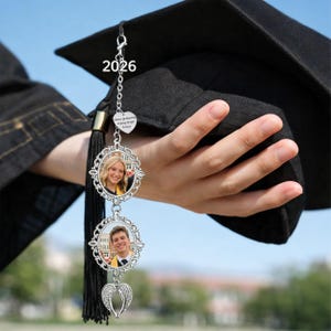Pu&ograve; includere: Un ciondolo a nappa per la laurea con due cornici ovali per foto e un ciondolo a forma di cuore con la scritta "Happy Graduation, Wishing Brighter Future!". &Egrave; appeso a un cappello di laurea nero. L'anno "2026" &egrave; stampato sul cappello.