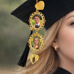 Pu&ograve; includere: Ciondolo per nappa di laurea dorato con due cornici ovali per foto e un ciondolo a forma di cuore. Le cornici contengono foto di un giovane uomo e una giovane donna. Il ciondolo a forma di cuore riporta la scritta "Believe in yourself, chase your dreams."