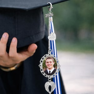 Pu&ograve; includere: Un ciondolo per nappa di cappello di laurea con una foto in una cornice d'argento decorativa. Il ciondolo include un cuore d'argento con la scritta "Believe in yourself, chase your dreams" e un ciondolo ad ala d'angelo d'argento.