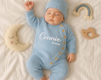 May include: A sleeping baby wearing a light blue knit romper and matching beanie with a pom-pom. The romper has the name "Connie" embroidered on it. Yellow buttons accent the side closure. A crescent moon and rainbow-shaped toy are nearby.
