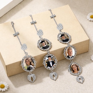 May include: Three silver graduation photo ornaments. Each ornament has a photo in an oval frame, a heart-shaped charm with text, and a charm with the year "2026". The bottom of each ornament has a pair of angel wings.