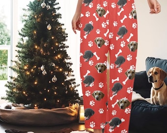 May include: Red pajama pants with a repeating pattern of dog faces, white paw prints, and bones. The pajama pants are loose-fitting and have a comfortable design. A Christmas tree is in the background.
