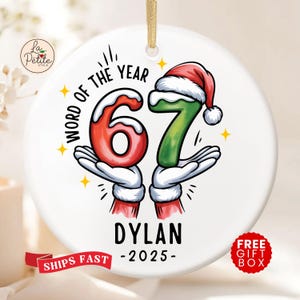 May include: A white ceramic Christmas ornament with a gold string for hanging. The ornament features the text "WORD OF THE YEAR" and the numbers "67" in red and green, held by cartoon hands. The name "DYLAN" and the year "-2025-" are also displayed.