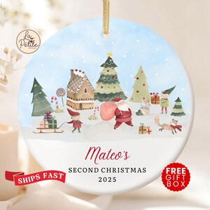 May include: Round Christmas ornament with a winter scene featuring Santa Claus, elves, and a gingerbread house. The ornament has the text "Mateo's Second Christmas 2025". A gold string is attached for hanging.
