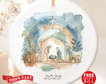 May include: White ceramic Christmas ornament with a gold string for hanging. The ornament features a watercolor-style illustration of the Nativity scene with a rainbow, stars, and the year 2025.