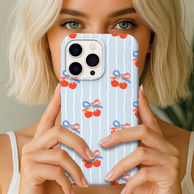 May include: A light blue phone case with a repeating pattern of red cherries and blue bows. The case has a vertical striped background. The phone case is designed to fit a smartphone.