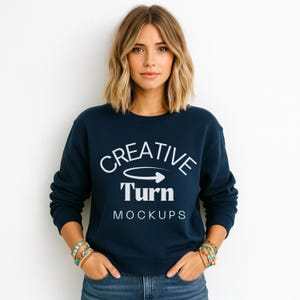 May include: Navy blue sweatshirt with the text "CREATIVE Turn MOCKUPS" in white. The sweatshirt has a crew neck and long sleeves. The model is wearing bracelets on both wrists.