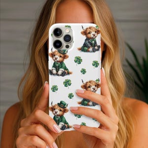 May include: White phone case featuring a repeating pattern of cartoon Highland cows dressed in green St. Patrick's Day outfits, including jackets and hats, with green shamrocks scattered across the surface.