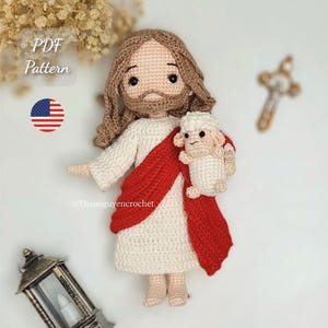 Op de afbeelding: Gehaakte pop van Jezus met bruin haar en baard, gekleed in een wit gewaad en een rode sjerp, met een klein wit lammetje. De pop heeft een zachte uitdrukking. De afbeelding bevat de tekst "PDF Pattern" en de Amerikaanse vlag.