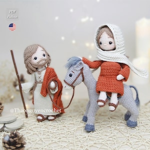 May include: Two crochet dolls representing a bearded figure in a beige robe with a rust-colored shawl holding a wooden staff, and a figure in a rust-colored tunic with a cream head covering riding a grey donkey with a blue mane and tail.
