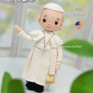 Puede incluir: Muñeca de ganchillo del Papa, con una túnica blanca, sombrero y zapatos negros. La muñeca tiene una cara sonriente y un collar con una cruz. La palabra "Pope" está escrita en letras blancas en la parte superior. El texto "PDF Pattern" también es visible.