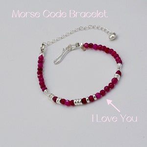 May include: A pink and silver beaded bracelet with a silver clasp and chain. The beads spell out "I Love You" in Morse code.