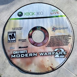 Puede incluir: Alfombra circular diseñada para parecerse a un disco de juego de Xbox 360 de "Call of Duty: Modern Warfare 2". La alfombra presenta el logotipo del juego, la clasificación ESRB y la marca Xbox. La alfombra tiene aproximadamente 91 cm de diámetro.