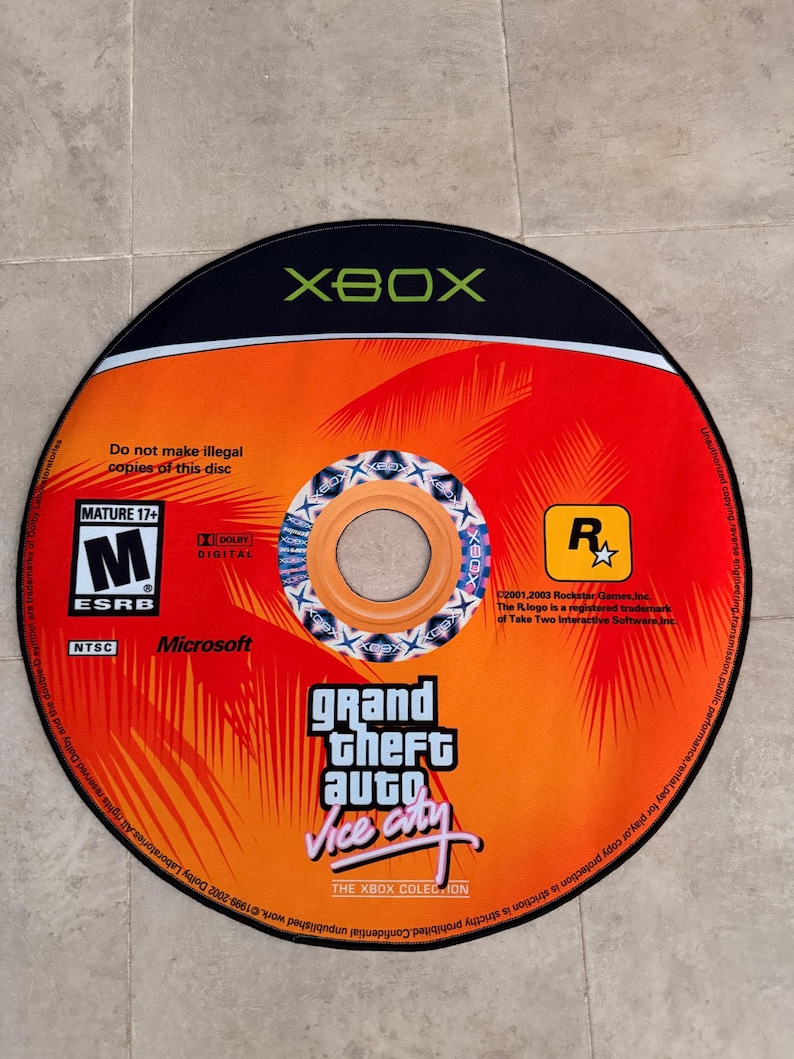 Puede incluir: Un disco negro de Xbox con un dise&ntilde;o naranja y rojo. El disco tiene el texto "Grand Theft Auto Vice City" y la clasificaci&oacute;n ESRB "M" para mayores de 17 a&ntilde;os.