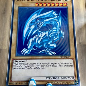 Puede incluir: Una carta de juego de rol "Drag&oacute;n Blanco de Ojos Azules" con un fondo azul claro. La carta representa un drag&oacute;n blanco con ojos azules sobre un fondo azul claro. El texto de la carta dice "Drag&oacute;n Blanco de Ojos Azules" y "[DRAGON]". La carta tambi&eacute;n incluye el texto "Este legendario drag&oacute;n es un poderoso motor de destrucci&oacute;n. Pr&aacute;cticamente invencible, muy pocos se han enfrentado a esta incre&iacute;ble criatura y han vivido para contarlo."
