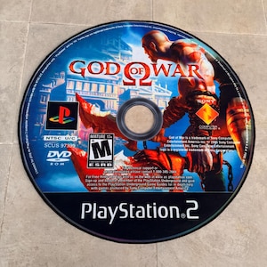 Puede incluir: Un disco de juego de PlayStation 2 para God of War II. El disco es negro con un logotipo de PlayStation 2 plateado y el t&iacute;tulo del juego en blanco. El disco presenta un fondo rojo y naranja con un personaje del juego, Kratos, en el centro.