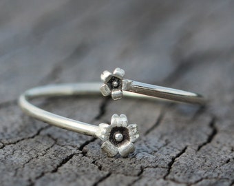 Könnte beinhalten: Ein silberner Ring mit zwei blütenförmigen Akzenten. Der Ring ist offen und verstellbar.