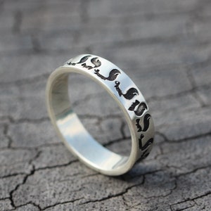 May include: A silver band ring with a black design of repeating shapes around the band.