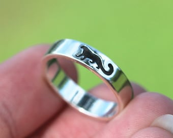 May include: A silver ring with a black silhouette of a cat on the band.