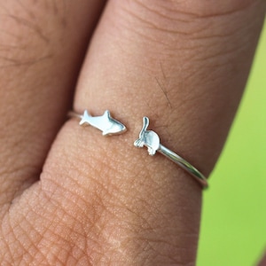 Op de afbeelding: Een zilveren ring met een haai- en konijnontwerp. De ring wordt gedragen aan een vinger.