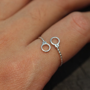 May include: A silver ring with two handcuff charms connected by a delicate chain. The ring is worn on a person's finger.