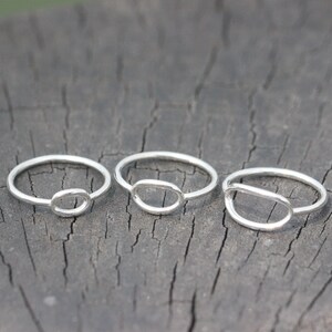 Op de afbeelding: Drie zilveren ringen met een eenvoudige ovale vorm uitgesneden uit de band. De ringen zijn gestapeld op een houten oppervlak.
