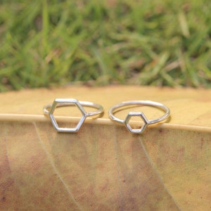 Puede incluir: Dos anillos hexagonales de plata sobre un fondo de hoja marrón. Los anillos son simples y minimalistas en diseño.