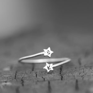以下が含まれることがあります： 星型のチャームが2つ付いたシルバーリング。チャームには「S」と「K」の文字が刻まれています。