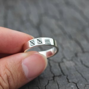 May include: A silver band ring with a simple design of three parallel lines engraved on the band.