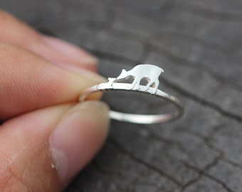 May include: A silver ring with a cutout design of a deer and fawn. The ring is on a finger.
