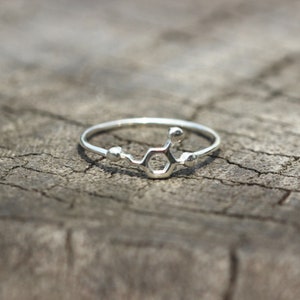 May include: A silver ring with a chemical structure design. The ring is on a wooden surface.