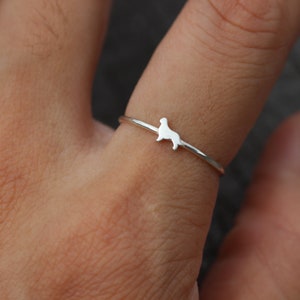 May include: A silver ring featuring a dainty silhouette of a dog. The ring is worn on a finger.