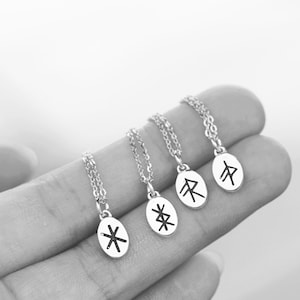 Puede incluir: Cuatro collares de plata con colgantes ovalados que presentan diferentes runas nórdicas. Las runas están grabadas en tinta negra.