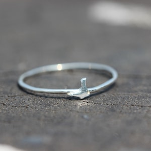 May include: A silver ring with a small bird design. The ring is thin and delicate.