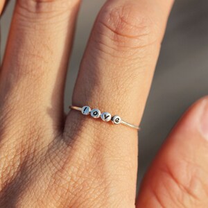 Può includere: Un anello d'argento con la parola "love" scritta in piccole perle.