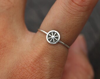 May include: A silver ring with a circular design featuring a stylized eight-pointed star.