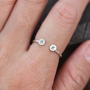 Op de afbeelding: Een zilveren ring met twee ronde bedels, een met de letter "B" en de andere met de letter "E".