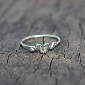 Könnte beinhalten: Ein silberner Schlangenring mit schlichtem Design. Der Ring liegt auf einer rustikalen Holzoberfläche.