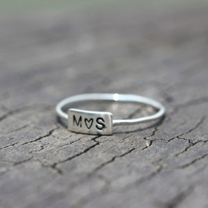 Könnte beinhalten: Ein silberner Ring mit einem rechteckigen Band, auf dem die Buchstaben "M♥S" eingraviert sind.