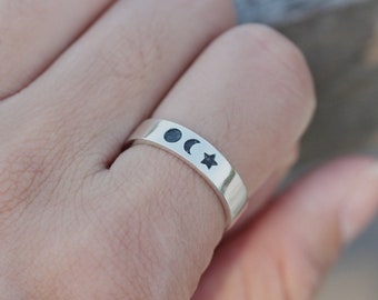 May include: A silver ring with a crescent moon, full moon, and star design.