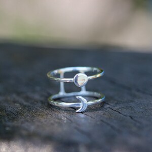 May include: A silver ring with a crescent moon and a small circle design. The ring is made of two bands that are connected together.