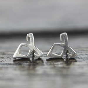 May include: A pair of silver earrings with a geometric design. The earrings are small and delicate, and they have a modern look.